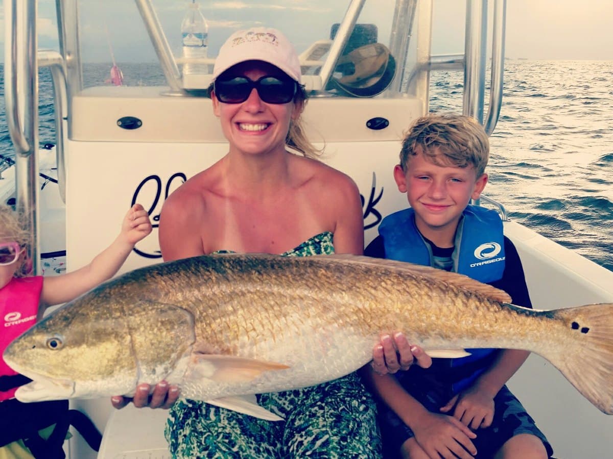 Angler and two kids on a center console holding a big bull redfish