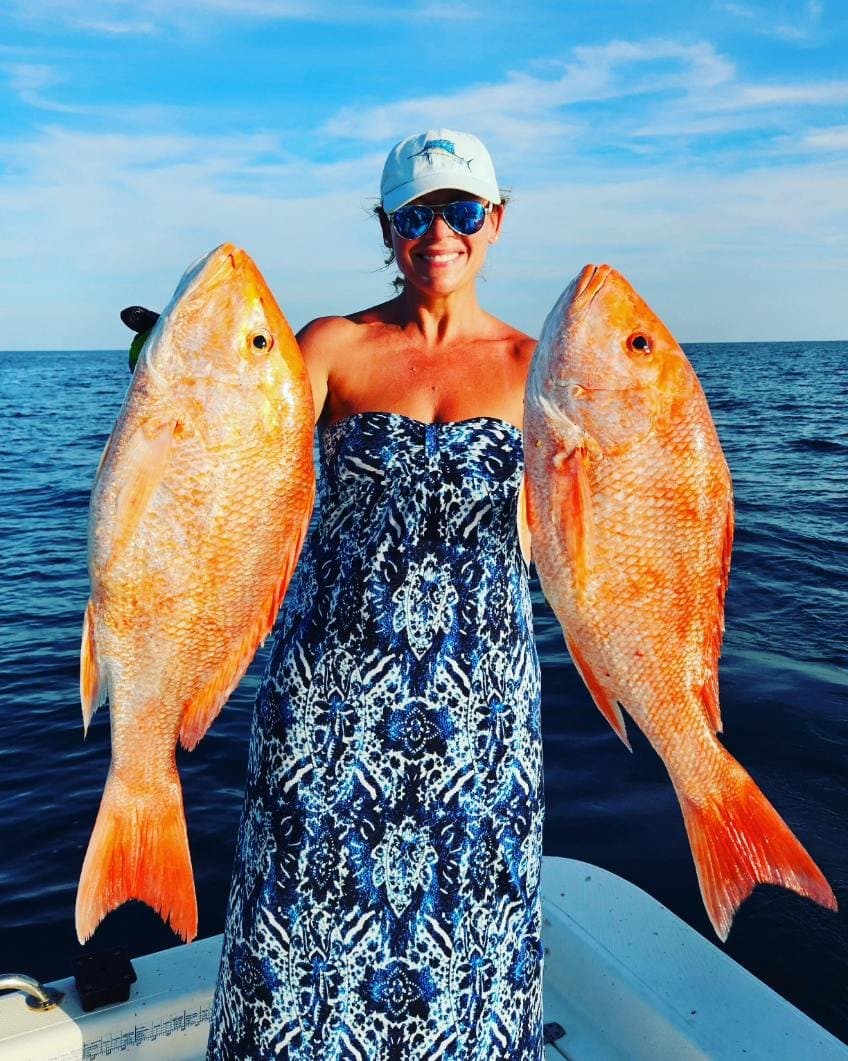 Angler on a boat offshore holding up two big red snapper